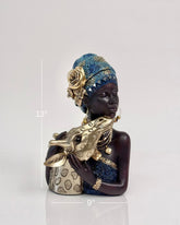 High Objects Serenity Bond Woman & Giraffe Showpiece, a dark-skinned woman in a blue and gold headwrap and dress, embracing a golden giraffe.