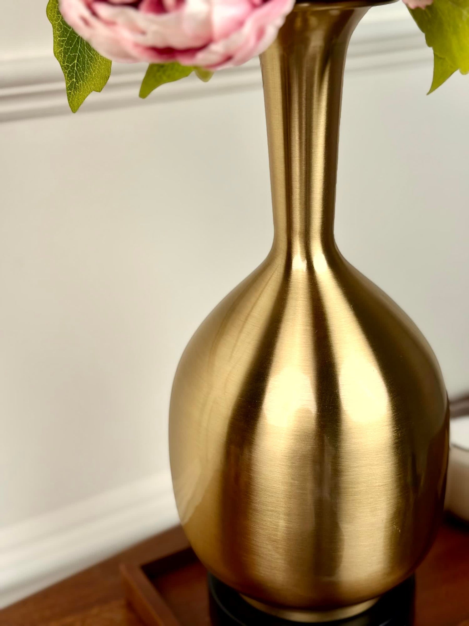 High Objects Solara Sculpted Vase in brushed gold metal with a rounded body and slender neck, displaying pink flowers.