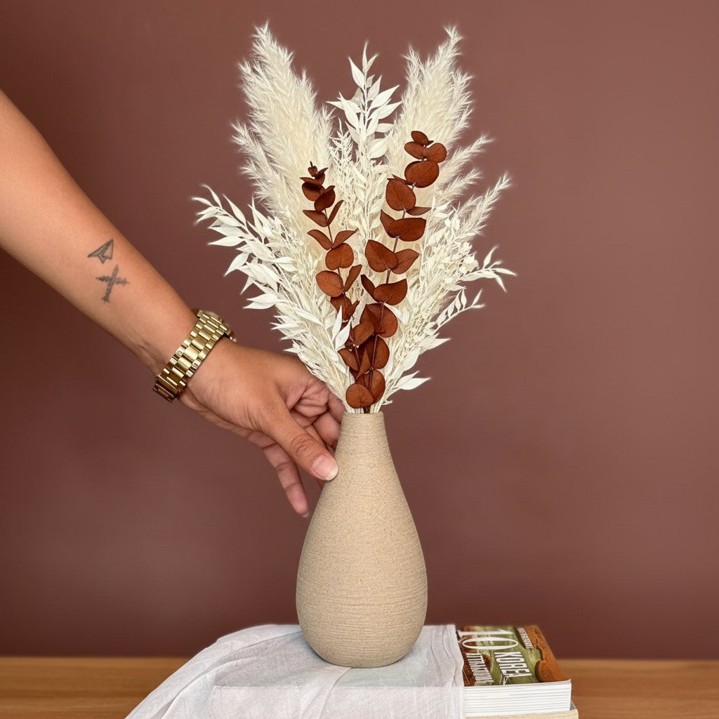 High Objects Solora Vase, a teardrop-shaped natural clay vase with a textured finish, holding dried bunny tail stems in tan and mint green.
