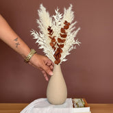 High Objects Solora Vase, a teardrop-shaped natural clay vase with a textured finish, holding dried bunny tail stems in tan and mint green.