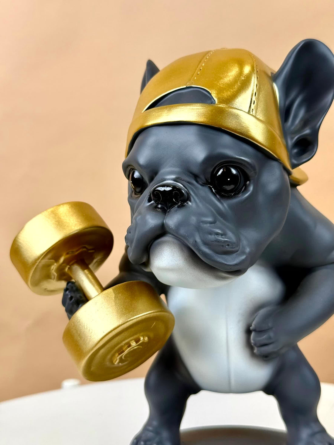 High Objects Sport Bulldog showpiece in matte black and grey, lifting a gold dumbbell and wearing a gold backward cap.