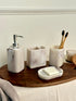 High Objects Stoneaura bathroom accessory set with soap dispenser, toothbrush holder, soap dish, and cup in marbled beige and white resin.