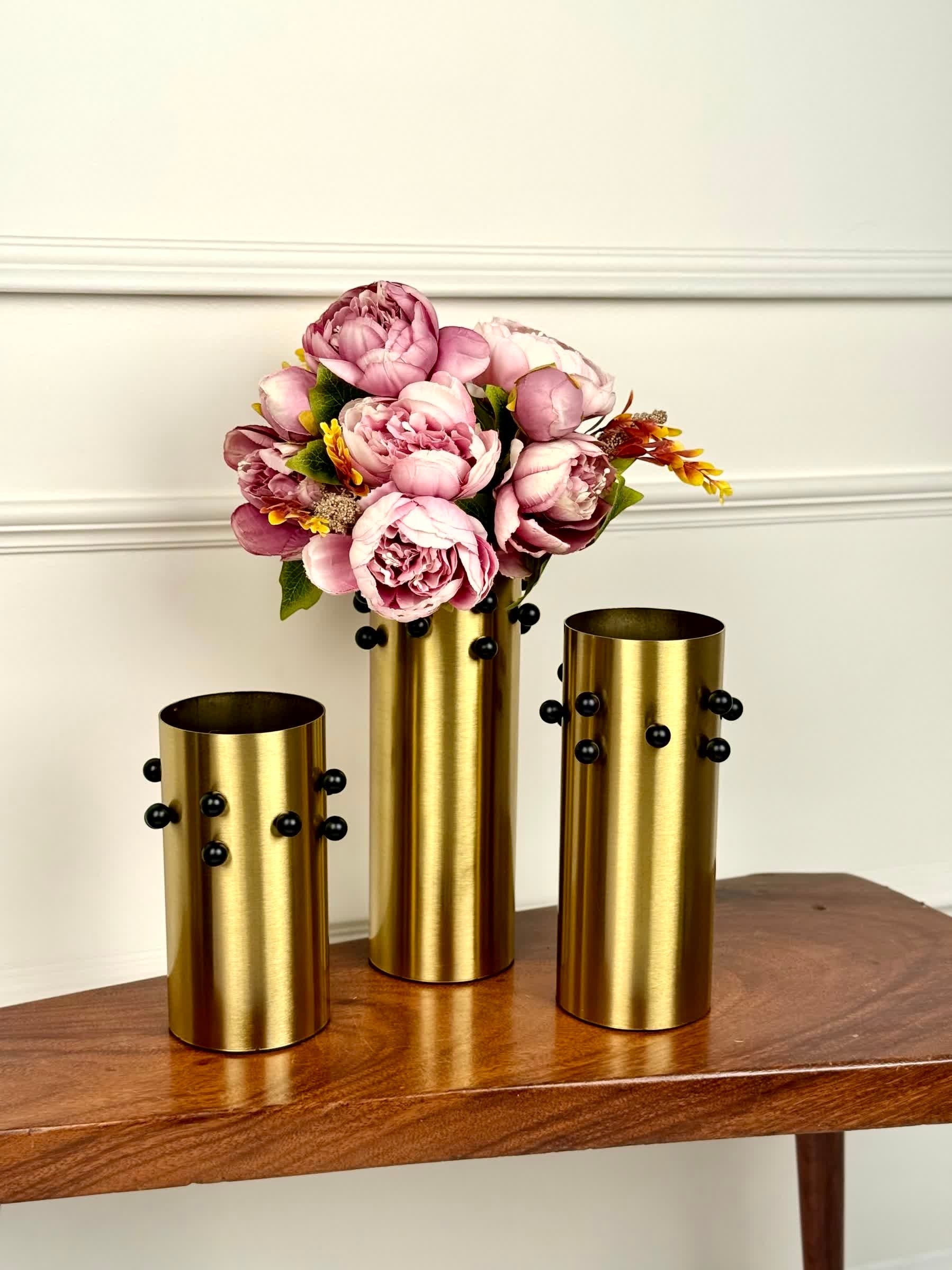 High Objects Studform Metal Vase set in brushed gold with black studs. Cylindrical vases with modern silhouette, one holding pink peonies.