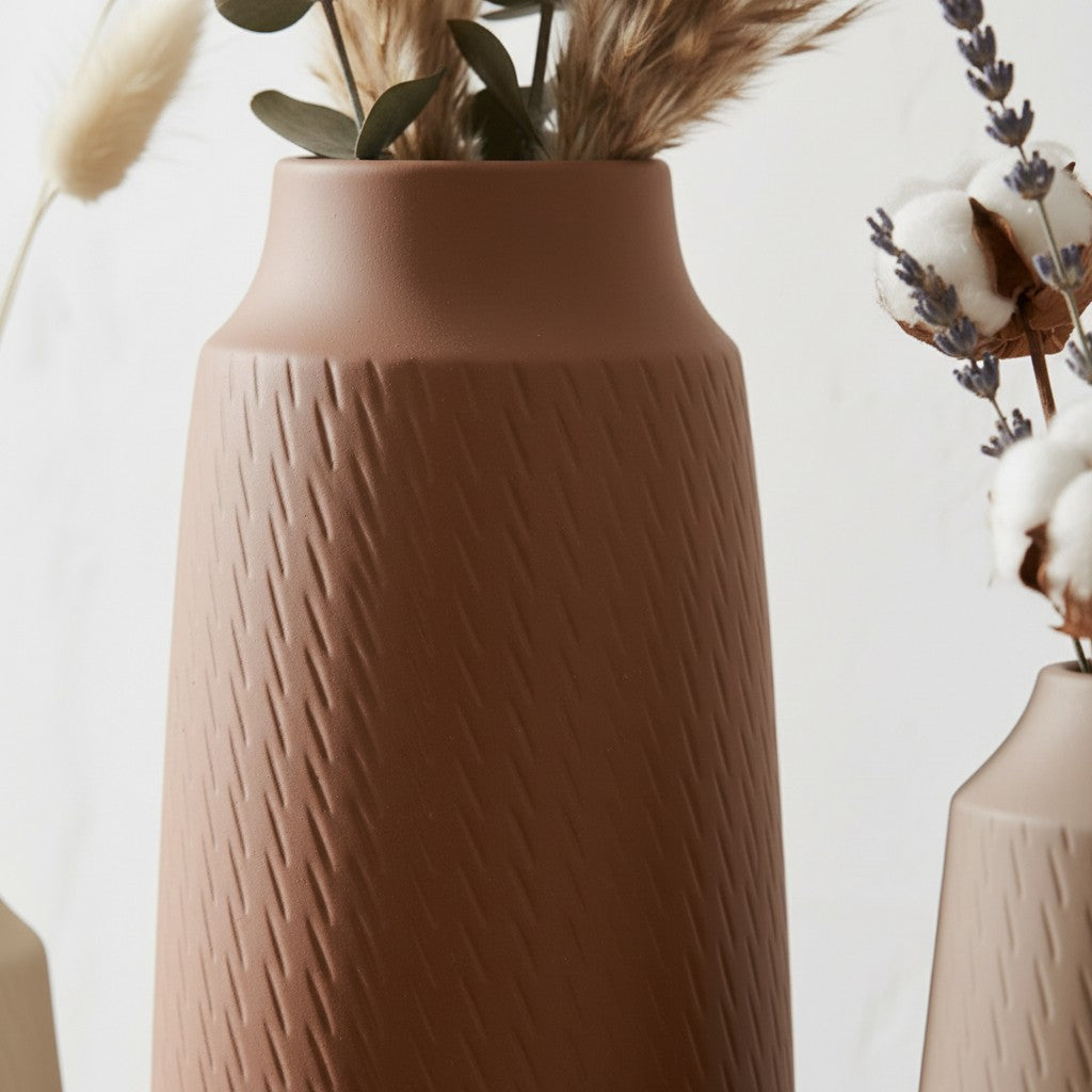 High Objects set of three textured ceramic vases in cream, terracotta, and beige, holding dried floral arrangements.