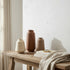 High Objects set of three textured ceramic vases in cream, terracotta, and beige, holding dried floral arrangements.