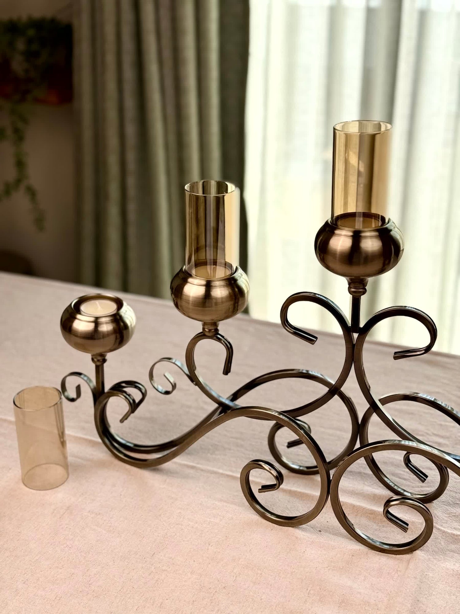 High Objects Valencia Scroll Five-Arm Candle Stand in antique bronze with amber glass holders. Features ornate scrollwork.