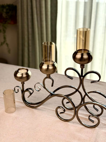 High Objects Valencia Scroll Five-Arm Candle Stand in antique bronze with amber glass holders. Features ornate scrollwork.