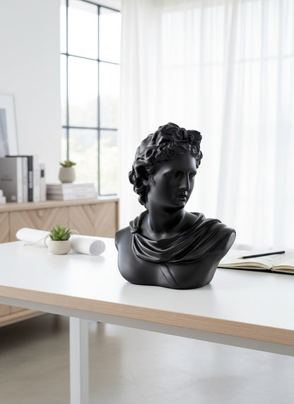 High Objects black matte bust of Apollo, a classical sculpture with intricate hair and draped clothing, displayed on a white desk.